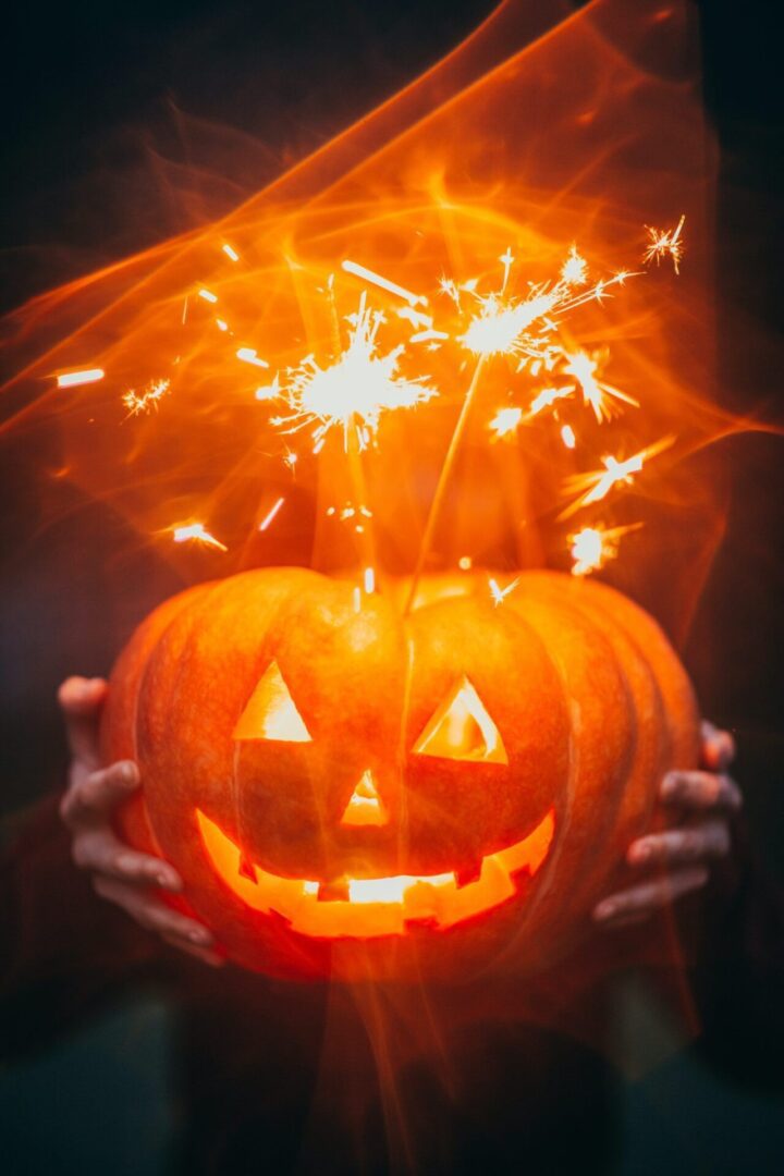 Hands holding illuminated pumpkin and sparklers
