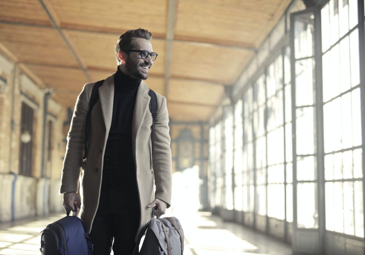 Traveler in coat holding bags indoors