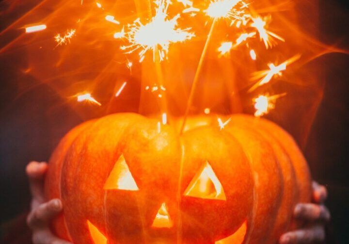Hands holding illuminated pumpkin and sparklers